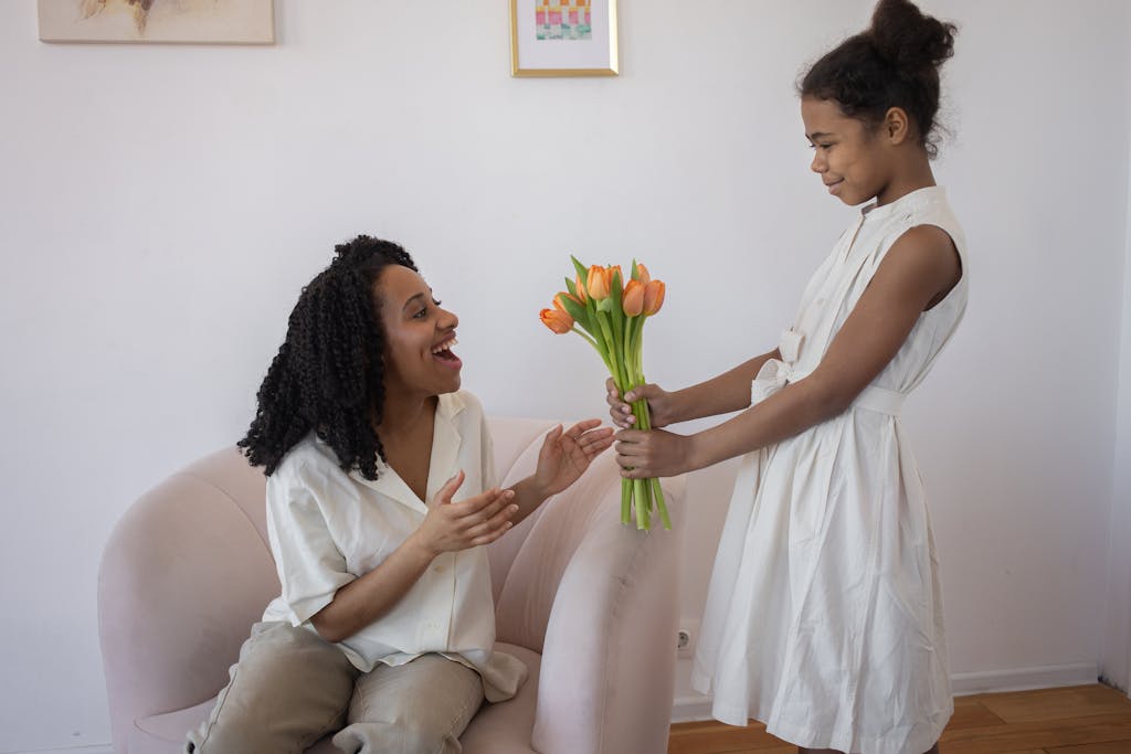A daughter surprises her mother with a bouquet of tulips at home, capturing love and happiness.